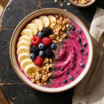 Smoothie bowl de frutas vermelhas em tigela branca, decorado com morango, mirtilo, framboesa e granola