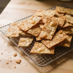 Biscoitos salgados de mandioca crocantes e dourados com gergelim, empilhados sobre grade de resfriamento