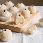 Beijinhos veganos cobertos de coco ralado com cravo no topo, em forminhas de papel sobre tábua de madeira